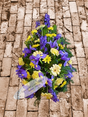 A funeral spray that features yellow and blue flowers with green foliage telford florist