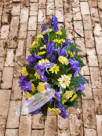 A funeral spray that features yellow and blue flowers with green foliage telford florist